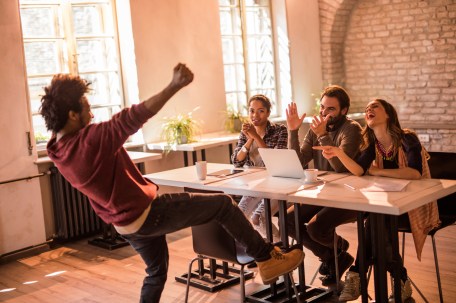 Group of happy business people congratulating cheerful African American man on getting a job at their office.