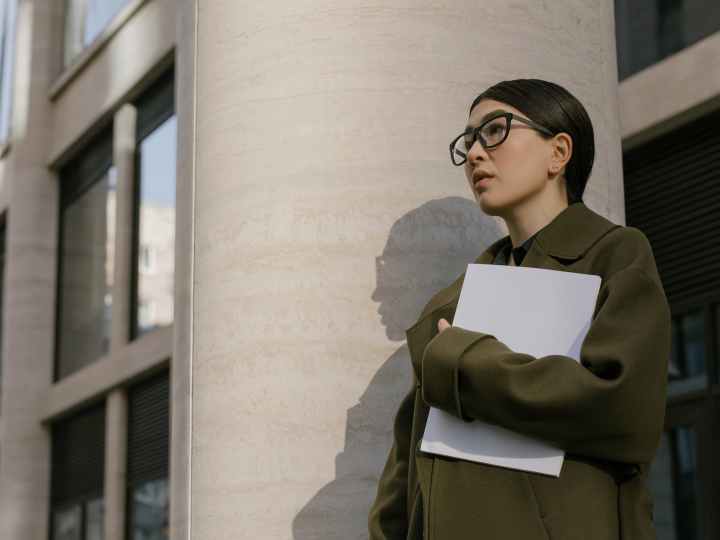 woman in black framed eyeglasses and green coat near the wall
