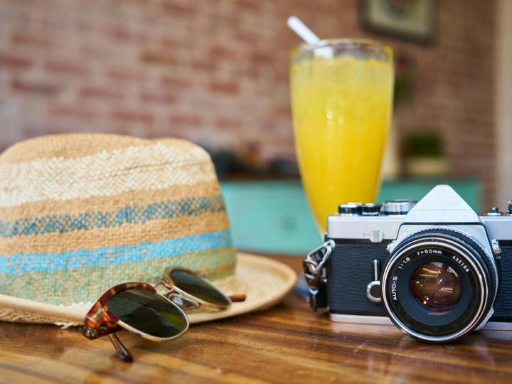 gray and black dslr camera beside sun hat and sunglasses